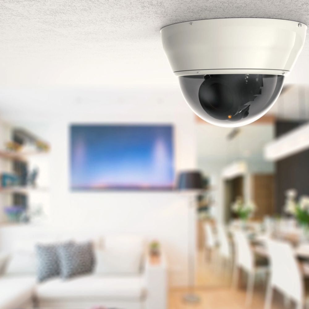 <span class="uk-h4">Indoor dome security camera installed on a white ceiling, monitoring a stylish, open-concept living and dining area with modern furniture.</span>