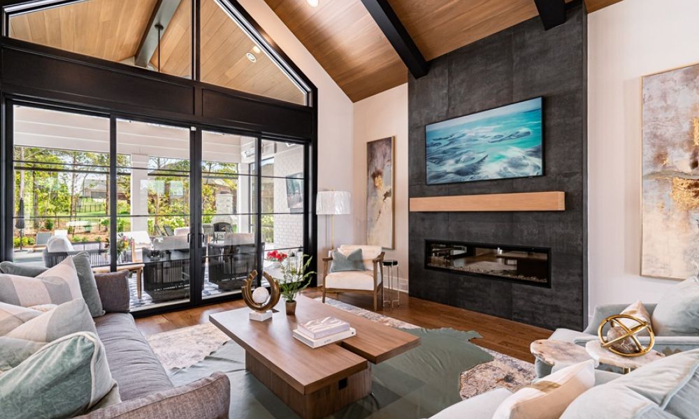 <span class="uk-h4">Modern living room with a wall-mounted TV over a black fireplace, vaulted wood ceilings, and large glass patio doors.</span>