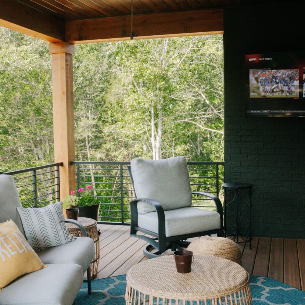 <span class="uk-h4">Covered patio with comfortable seating, a blue rug, and a large TV mounted on a dark brick wall.</span>
