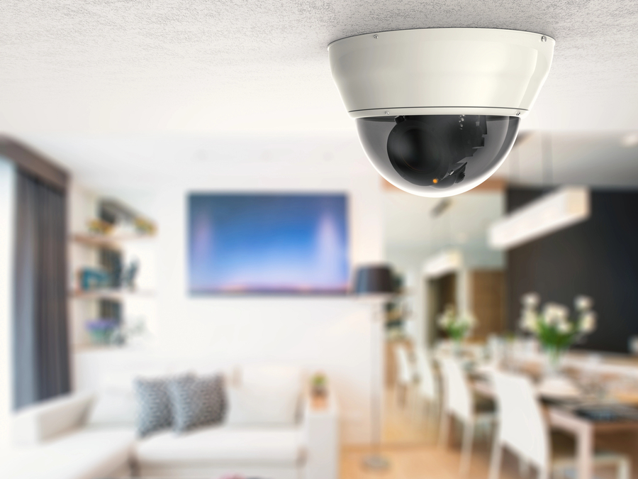 Indoor dome security camera installed on a white ceiling, monitoring a stylish, open-concept living and dining area with modern furniture.
