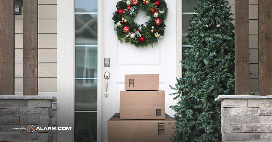 Packages stacked on front steps, behind it a white door with a smart lock and wreath. In the corner it reads ‘Power by Alarm.com’