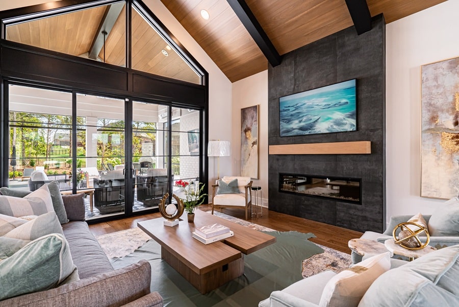 Modern living room with a wall-mounted TV over a black fireplace, vaulted wood ceilings, and large glass patio doors.